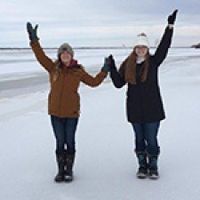 Two females students standing outide in the snow holding up their arms to make a giant "W"