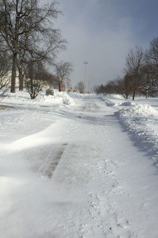 Photo of an empty campus sidewalk being covered over by drifting snow.