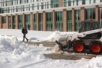 Photo of a small bulldozer scraping snow from the sidewalk in front of Sangren Hall.