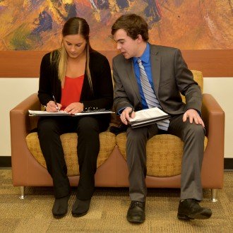 Photo of two students talking to one another as they jot down notes during a career fair.