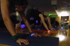 Photo of a row of people wearing various-colored glow sticks while exercising in a darkened room.