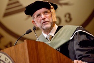 Photo of WMU President John M. Dunn, dressed in academic regalia, speaking at a commencement ceremony.