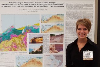 Photo of VanderMeer posing with a huge poster that describes her research through text as well as colorful drawings and photos.