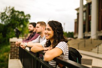 Photo of three WMU students leaning over a railing atop the hill near East Hall.