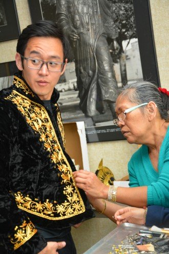 A Malaysian students receives help with his clothing from an older Malaysian community member.