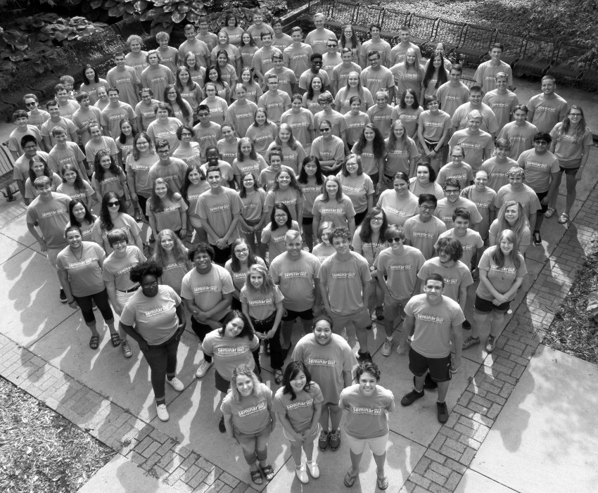 A black and white photo of a group of about 120 high school music camp students both male and female posing for a group picture in matching t-shirts.
